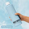 A hand holding a large light blue bottle of Mozi Wash Laundry Detergent against a sky-blue cloudy background. A label at the bottom left reads 'Malibu Mornings'.