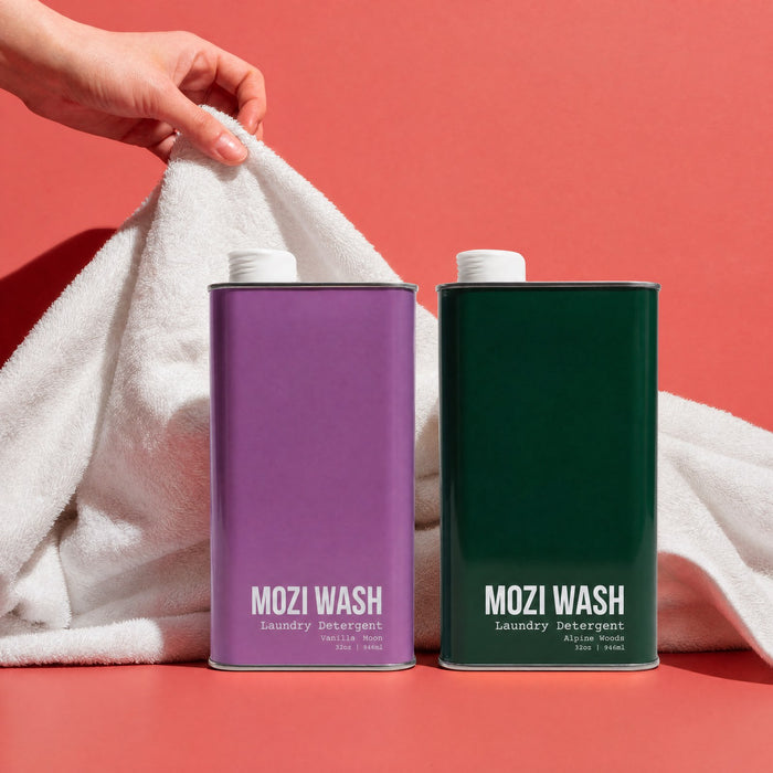 Hand lifting a white towel beside purple and green Mozi Wash detergent bottles